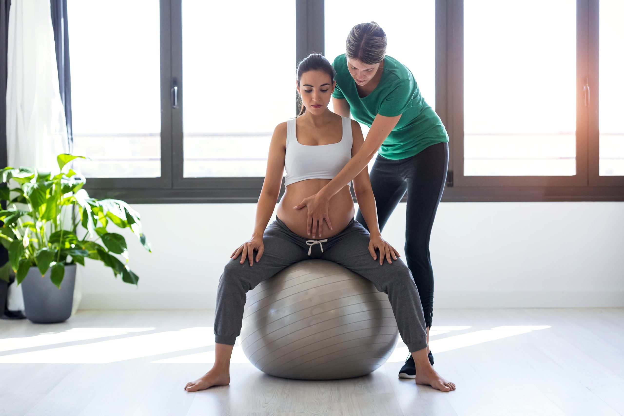 physiotherapist helping to beautiful pregnant woman for doing pi