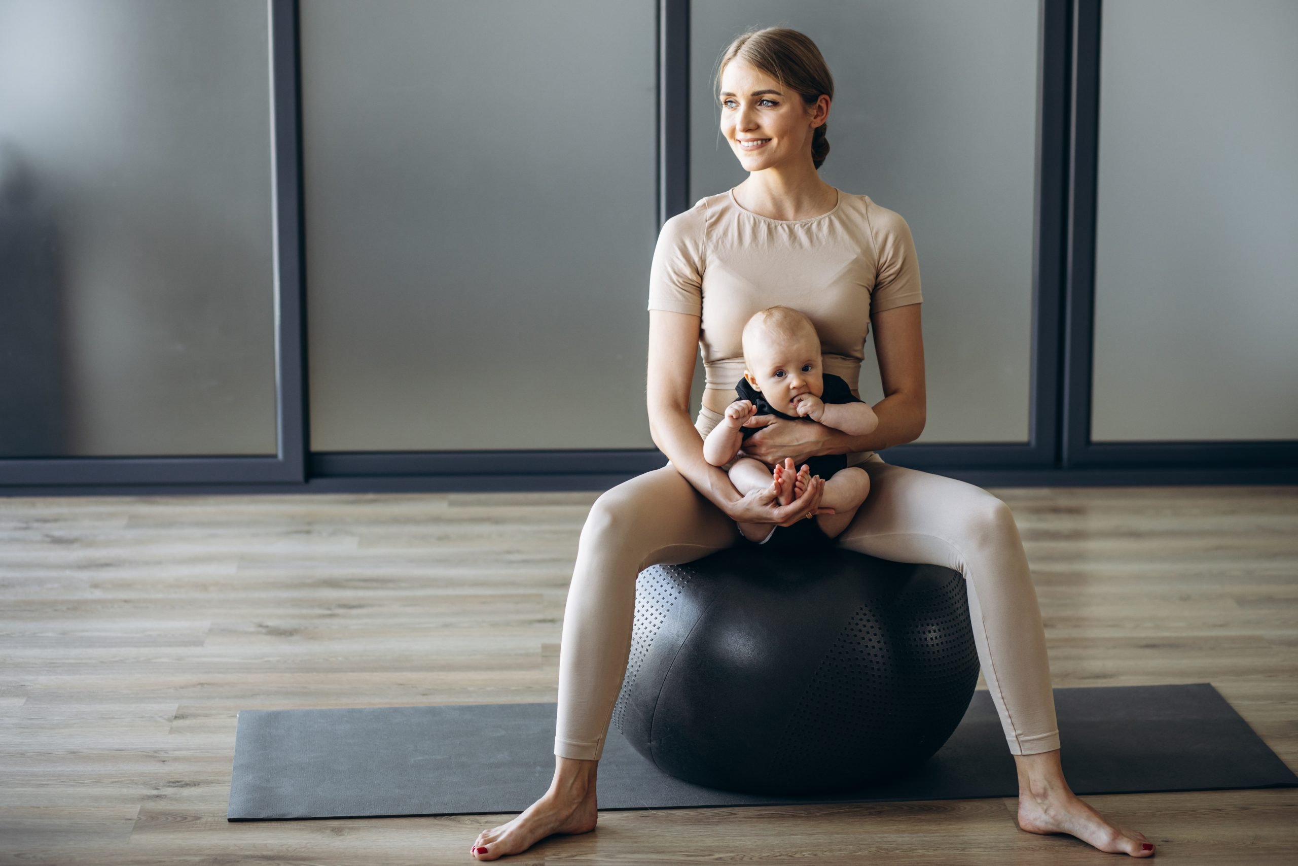 mother with baby daughter sitting on yoga ball